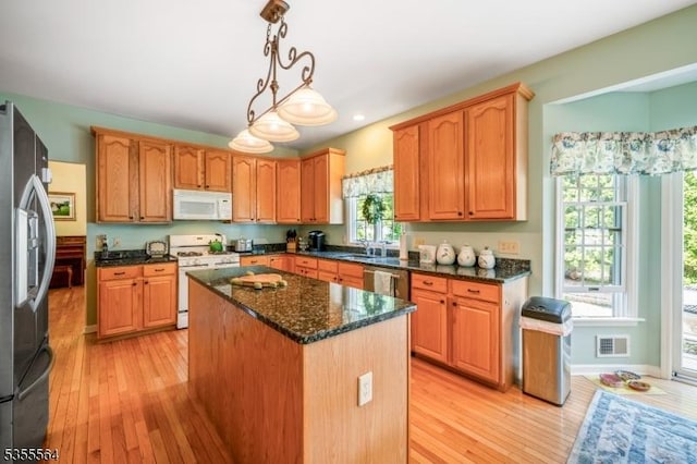 kitchen featuring stainless steel appliances, a center island, light wood-type flooring, a sink, and dark stone countertops