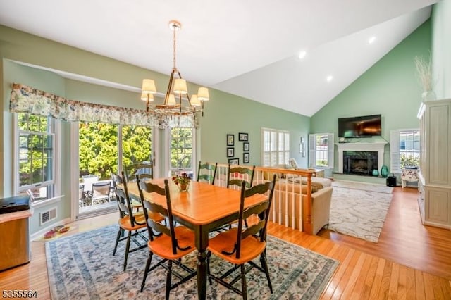 dining area with high vaulted ceiling, a chandelier, light wood-style flooring, a premium fireplace, and recessed lighting