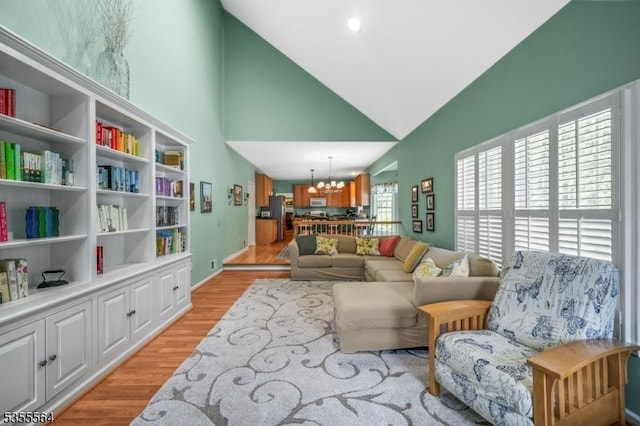 living room featuring a chandelier, high vaulted ceiling, light wood finished floors, and baseboards