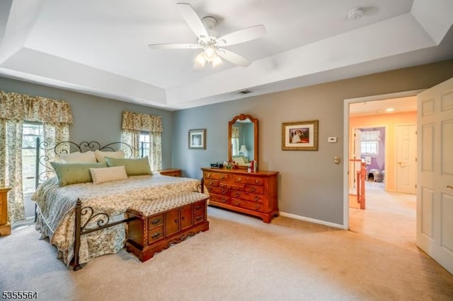 bedroom with a raised ceiling, light carpet, and multiple windows