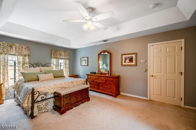 bedroom with a tray ceiling, multiple windows, light carpet, and baseboards