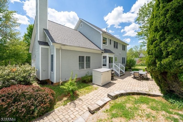 back of property featuring a patio, a chimney, and a shingled roof