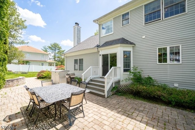 rear view of property featuring a patio area, fence, a chimney, and outdoor dining space