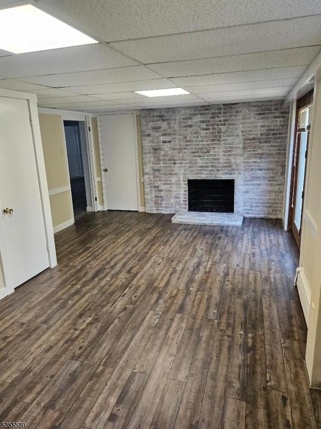 unfurnished living room featuring a drop ceiling, wood finished floors, a fireplace, and baseboards