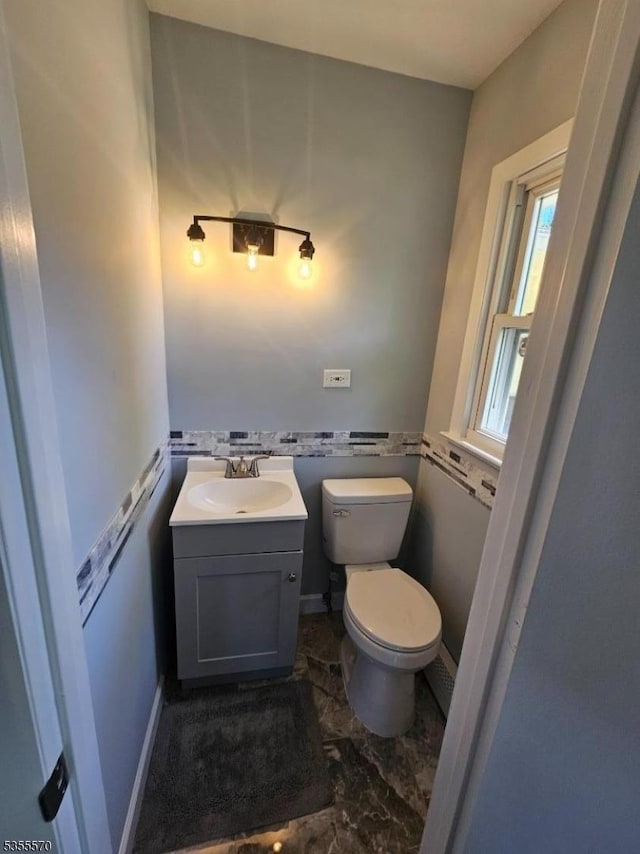 half bathroom with toilet, marble look tile flooring, and vanity