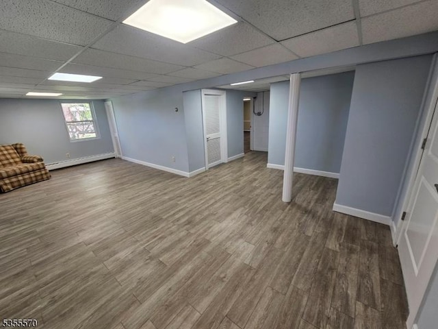 below grade area with a drop ceiling, wood finished floors, baseboards, and baseboard heating