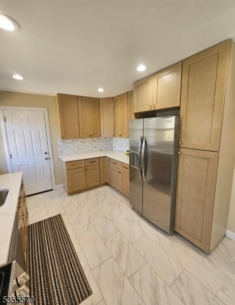 kitchen featuring stainless steel fridge with ice dispenser, light marble finish flooring, light countertops, recessed lighting, and baseboards