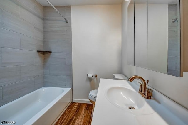 bathroom featuring toilet, wood finished floors, baseboards, shower / bathtub combination, and vanity