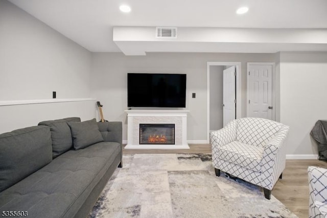 living room featuring light wood-style flooring, baseboards, recessed lighting, and a glass covered fireplace