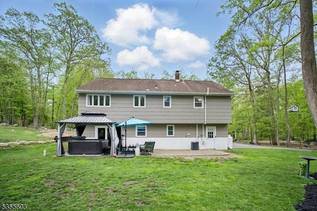 back of property featuring a hot tub, a patio area, a chimney, a gazebo, and a lawn