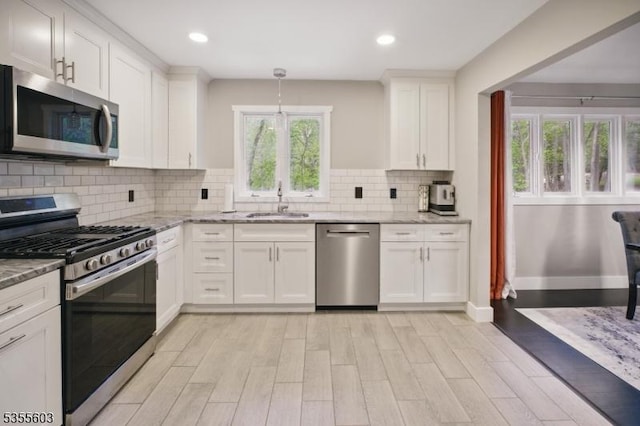 kitchen featuring stainless steel appliances, a sink, light wood-style flooring, light stone countertops, and white cabinetry