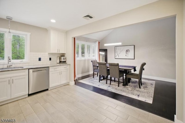 kitchen with stainless steel dishwasher, a sink, white cabinetry, healthy amount of natural light, and lofted ceiling