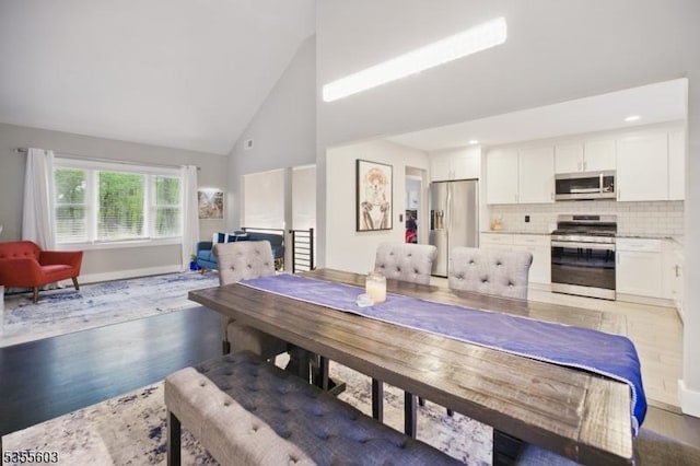 dining space featuring high vaulted ceiling, light wood-style floors, and baseboards