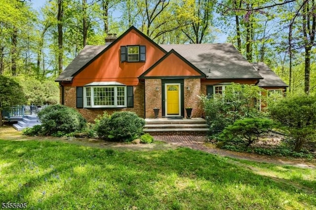 view of front of house featuring a front lawn, brick siding, a deck, and a shingled roof