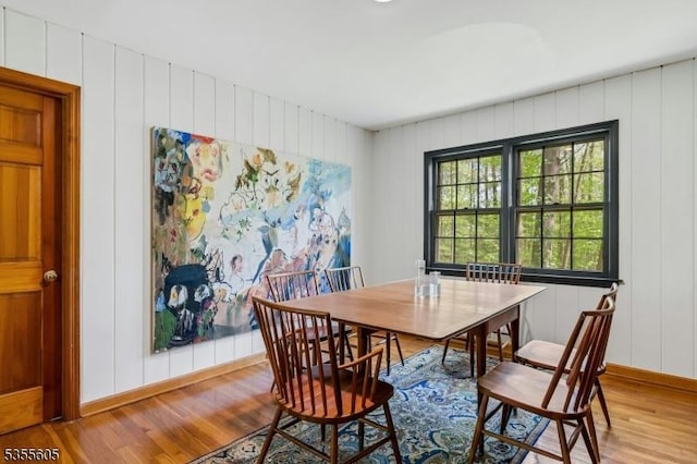 dining room featuring light wood-type flooring, baseboards, and a decorative wall