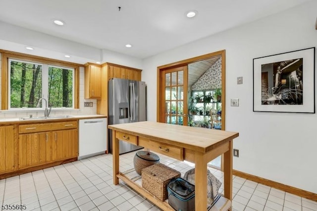 kitchen featuring white dishwasher, a sink, stainless steel fridge, light countertops, and plenty of natural light
