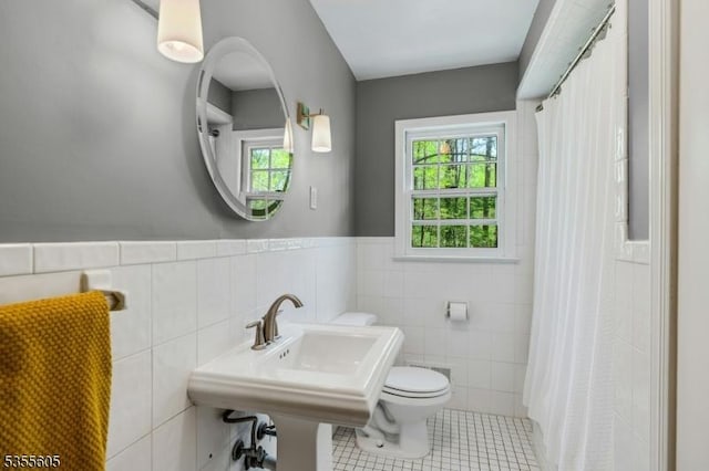 bathroom with tile walls, tile patterned floors, toilet, a wainscoted wall, and a shower with curtain
