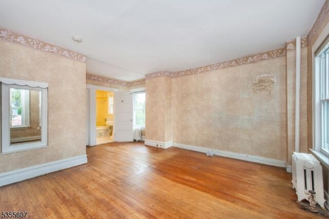 spare room with radiator heating unit, baseboards, light wood-type flooring, and healthy amount of natural light
