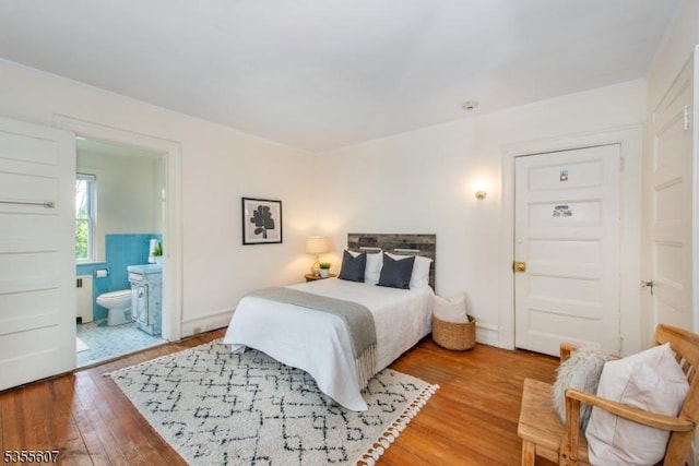 bedroom with light wood finished floors, radiator heating unit, and ensuite bathroom