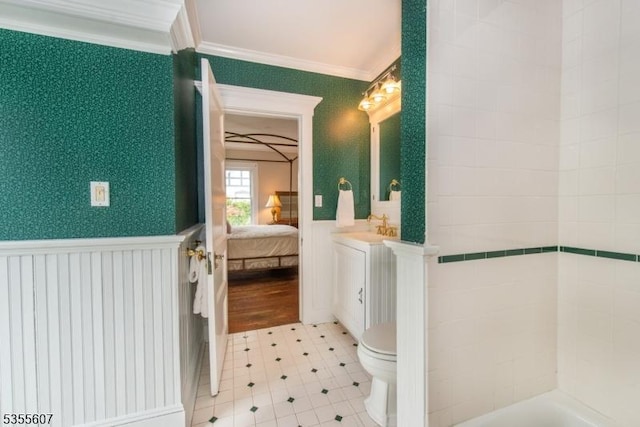 ensuite bathroom featuring ornamental molding, wainscoting, toilet, vanity, and a tub