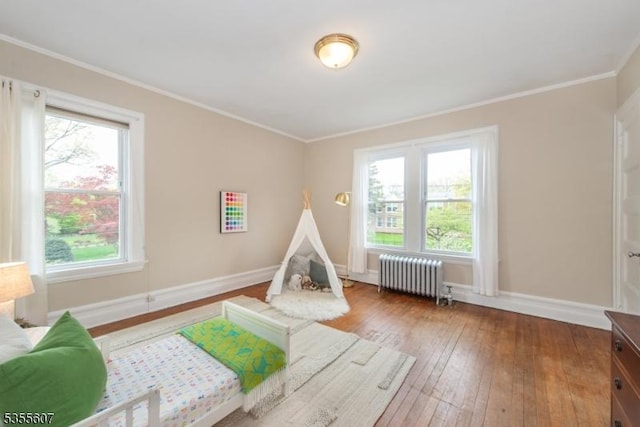 recreation room featuring radiator heating unit, healthy amount of natural light, baseboards, hardwood / wood-style flooring, and ornamental molding