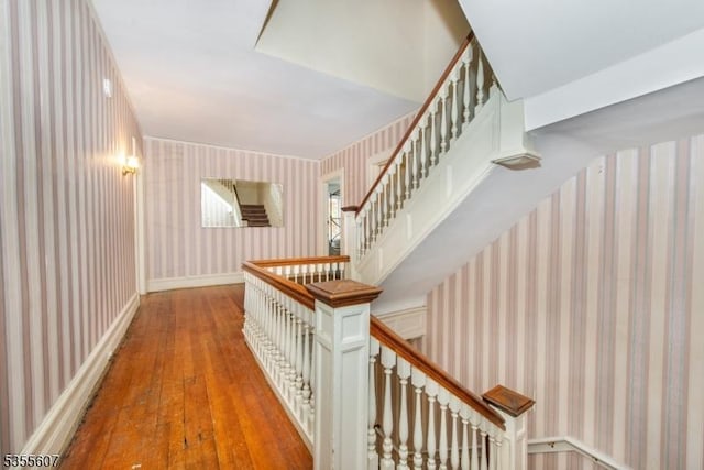 stairs with wallpapered walls and hardwood / wood-style flooring