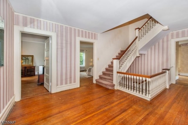 unfurnished living room with wallpapered walls, hardwood / wood-style flooring, stairs, and baseboards
