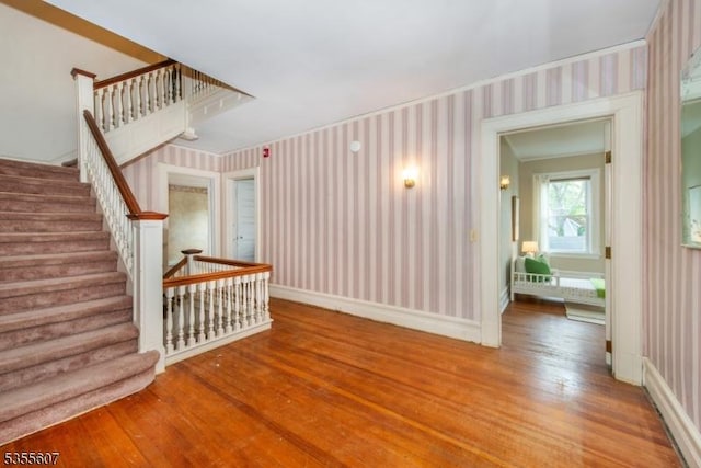 unfurnished living room featuring wallpapered walls, wood finished floors, stairs, and baseboards