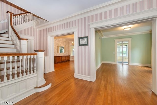 hallway featuring wallpapered walls, ornamental molding, wood finished floors, baseboards, and stairway