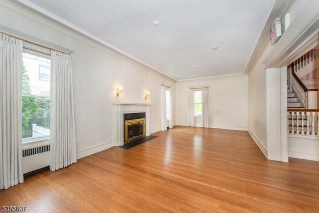unfurnished living room with light wood-style flooring, a fireplace with flush hearth, stairway, ornamental molding, and radiator heating unit