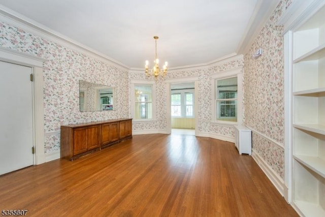 unfurnished dining area featuring a chandelier, wallpapered walls, radiator, wood finished floors, and ornamental molding