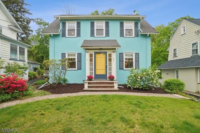 view of front facade with a front lawn, stucco siding, a chimney, and entry steps