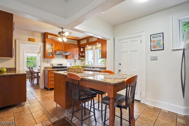 kitchen with brown cabinets, under cabinet range hood, stainless steel electric range oven, and plenty of natural light