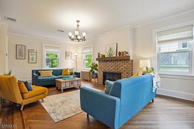 living area with a chandelier, a brick fireplace, radiator, ornamental molding, and wood finished floors