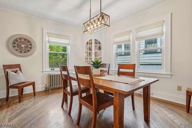 dining area featuring radiator, a chandelier, hardwood / wood-style flooring, ornamental molding, and baseboards