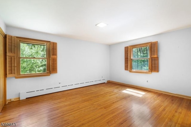empty room with a baseboard heating unit, a wealth of natural light, baseboards, and wood finished floors