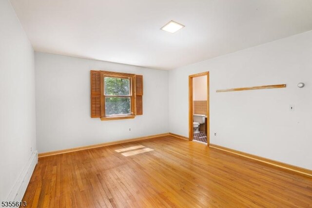 empty room with a baseboard radiator, light wood-style flooring, and baseboards
