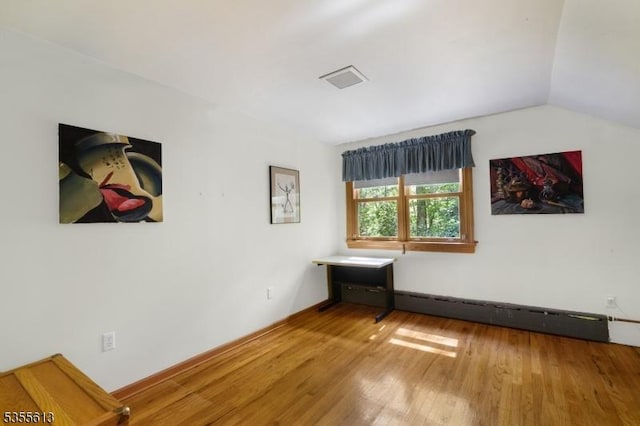 interior space with a baseboard heating unit, lofted ceiling, visible vents, and wood finished floors