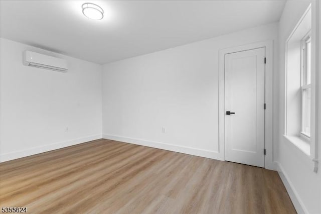 empty room with a wall mounted air conditioner, wood finished floors, and baseboards