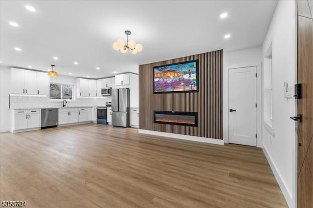 unfurnished living room with recessed lighting, light wood-style floors, a glass covered fireplace, and a notable chandelier