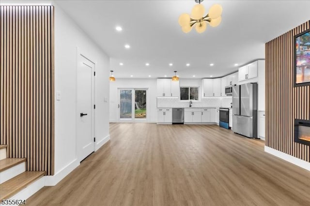 unfurnished living room featuring baseboards, recessed lighting, light wood-style flooring, a notable chandelier, and a glass covered fireplace