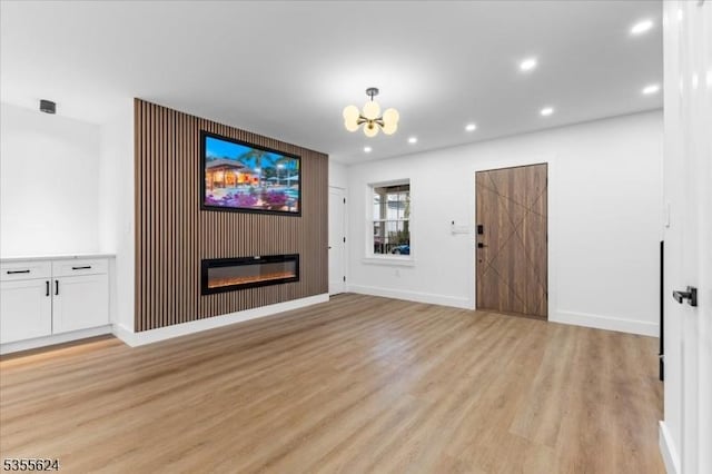 unfurnished living room with baseboards, a notable chandelier, light wood finished floors, and recessed lighting