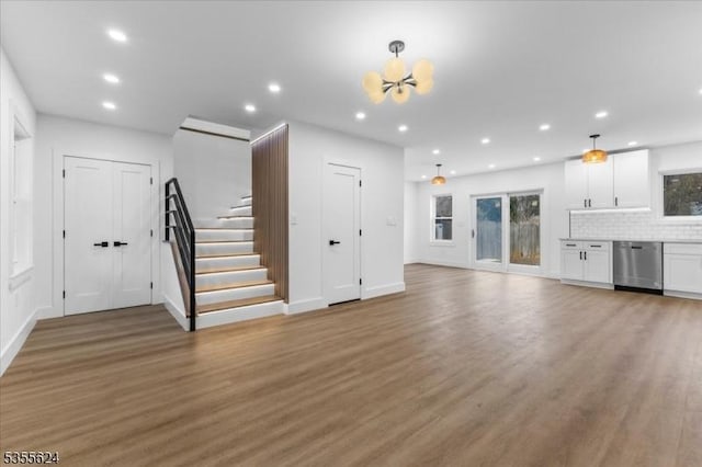 unfurnished living room featuring recessed lighting, baseboards, light wood finished floors, stairs, and a chandelier