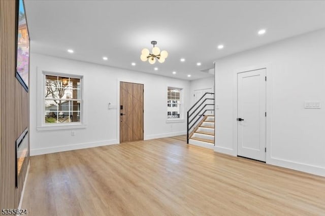 unfurnished living room featuring stairs, light wood finished floors, a healthy amount of sunlight, and a chandelier