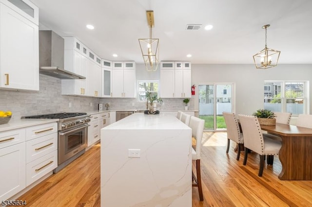 kitchen with a center island, wall chimney range hood, light wood-style floors, stainless steel appliances, and tasteful backsplash