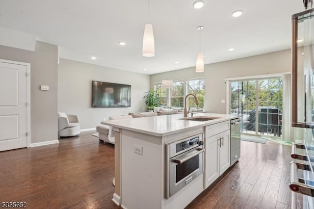 kitchen featuring stainless steel appliances, dark wood-style flooring, a sink, open floor plan, and light countertops