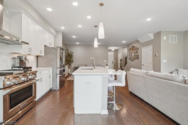 kitchen featuring a breakfast bar area, a sink, open floor plan, wall chimney range hood, and appliances with stainless steel finishes