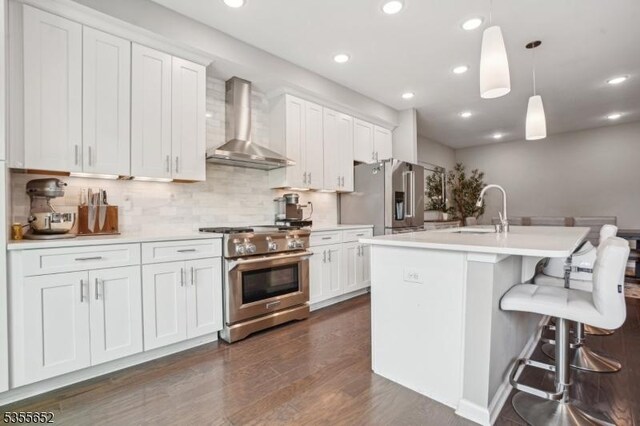 kitchen with a sink, high end appliances, wall chimney exhaust hood, light countertops, and recessed lighting