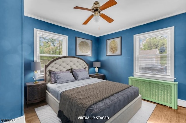bedroom with radiator, wood finished floors, crown molding, baseboards, and ceiling fan