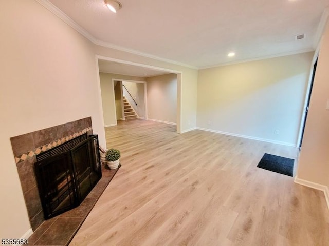 unfurnished living room with crown molding, light wood finished floors, a tile fireplace, stairs, and baseboards